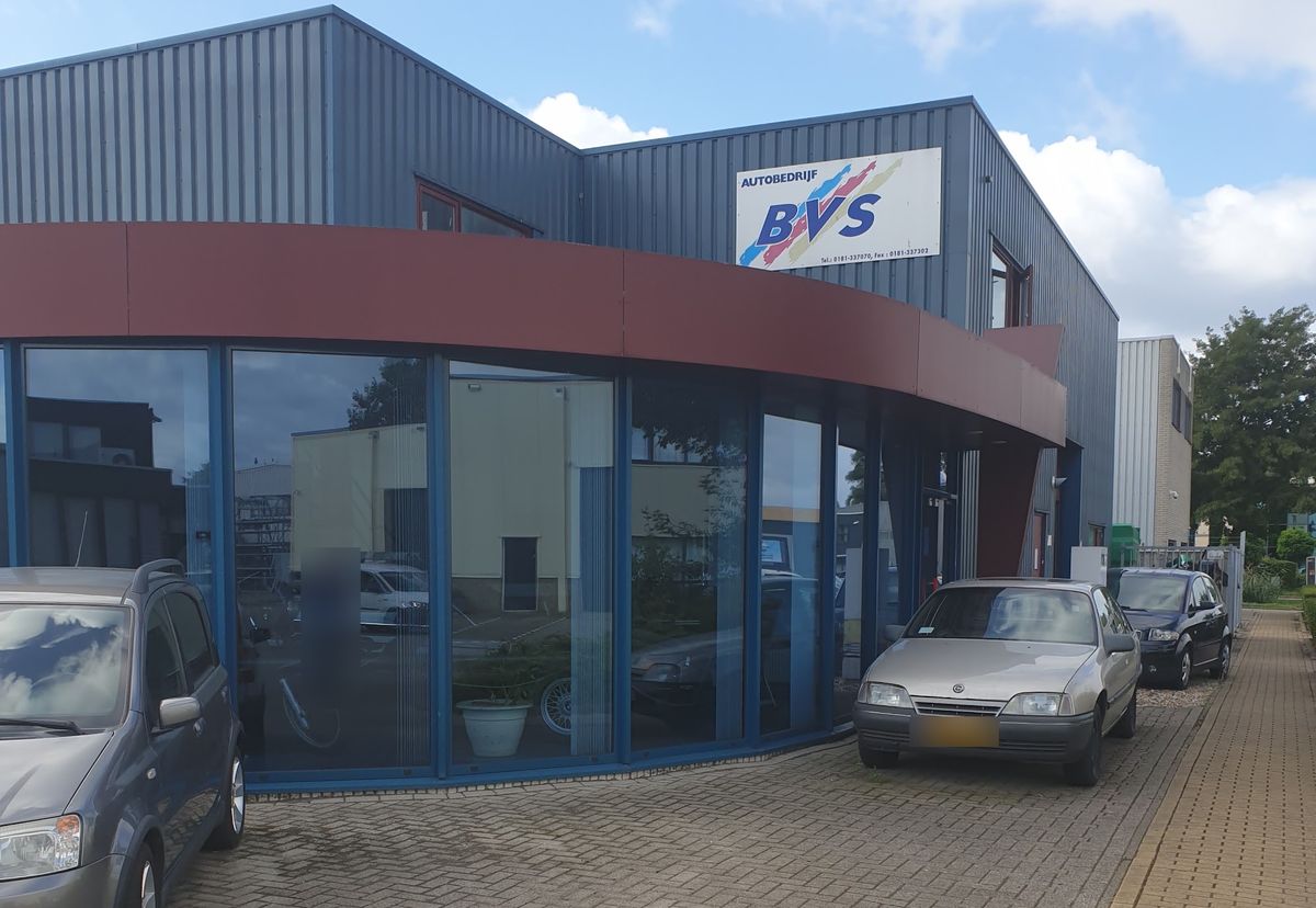 Het pand van Autobedrijf BVS: grijze hal met een rode band boven de ronde glazen pui en het BVS-bord
